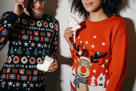 Paar in Weihnachtspullovern hält Weihnachtsplätzchen