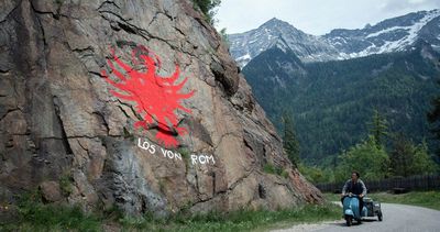 Paul (Thomas Prenn) fährt an einem Felsen mit dem Tiroler Adler und dem Schriftzug "Los von Rom" vorbei