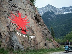 Paul (Thomas Prenn) fährt an einem Felsen mit dem Tiroler Adler und dem Schriftzug "Los von Rom" vorbei Paul (Thomas Prenn) fährt an einem Felsen mit dem Tiroler Adler und dem Schriftzug "Los von Rom" vorbei