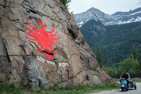 Paul (Thomas Prenn) fährt an einem Felsen mit dem Tiroler Adler und dem Schriftzug "Los von Rom" vorbei