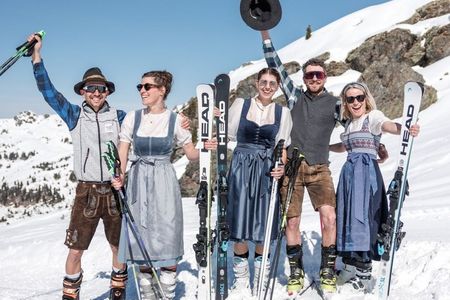 Personen in Tracht und auf Ski stehen gut gelaunt am Pistenrand